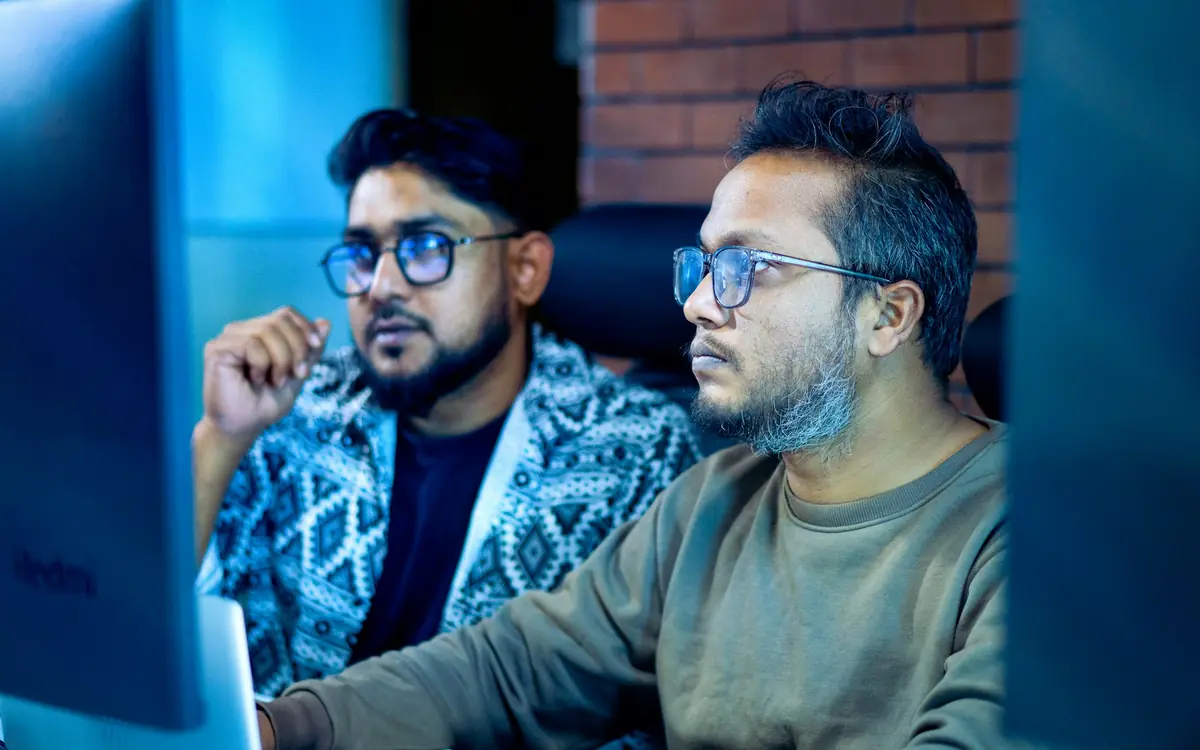 Two colleagues wearing glasses looking at one shared computer screen while reviewing business data together