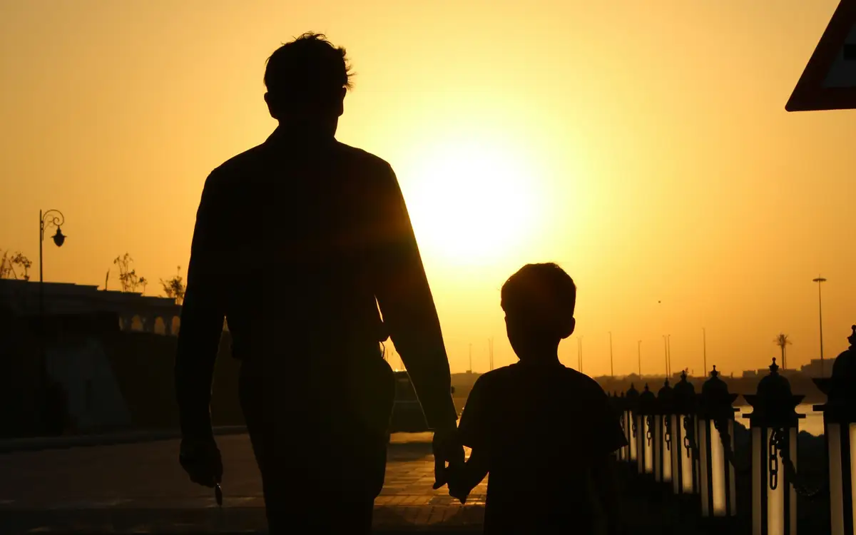 Silhouette of a father holding his young child's hand while walking at sunset, showing why parents want to keep track of their child's safety
