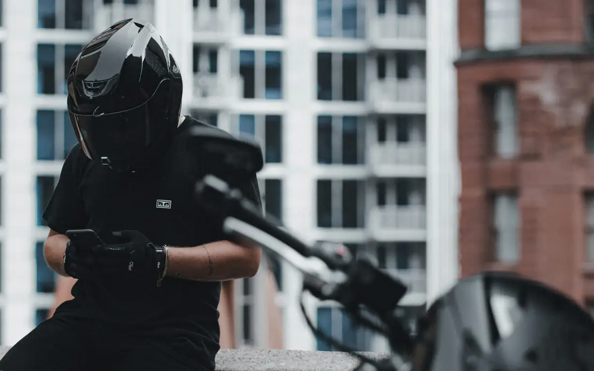 Motorcycle rider in a black helmet checking his phone beside his bike in a city street