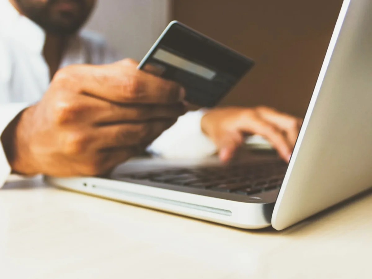 Close-up of a hand holding a credit card while typing on a laptop keyboard, representing GiveTurn's e-commerce solution service