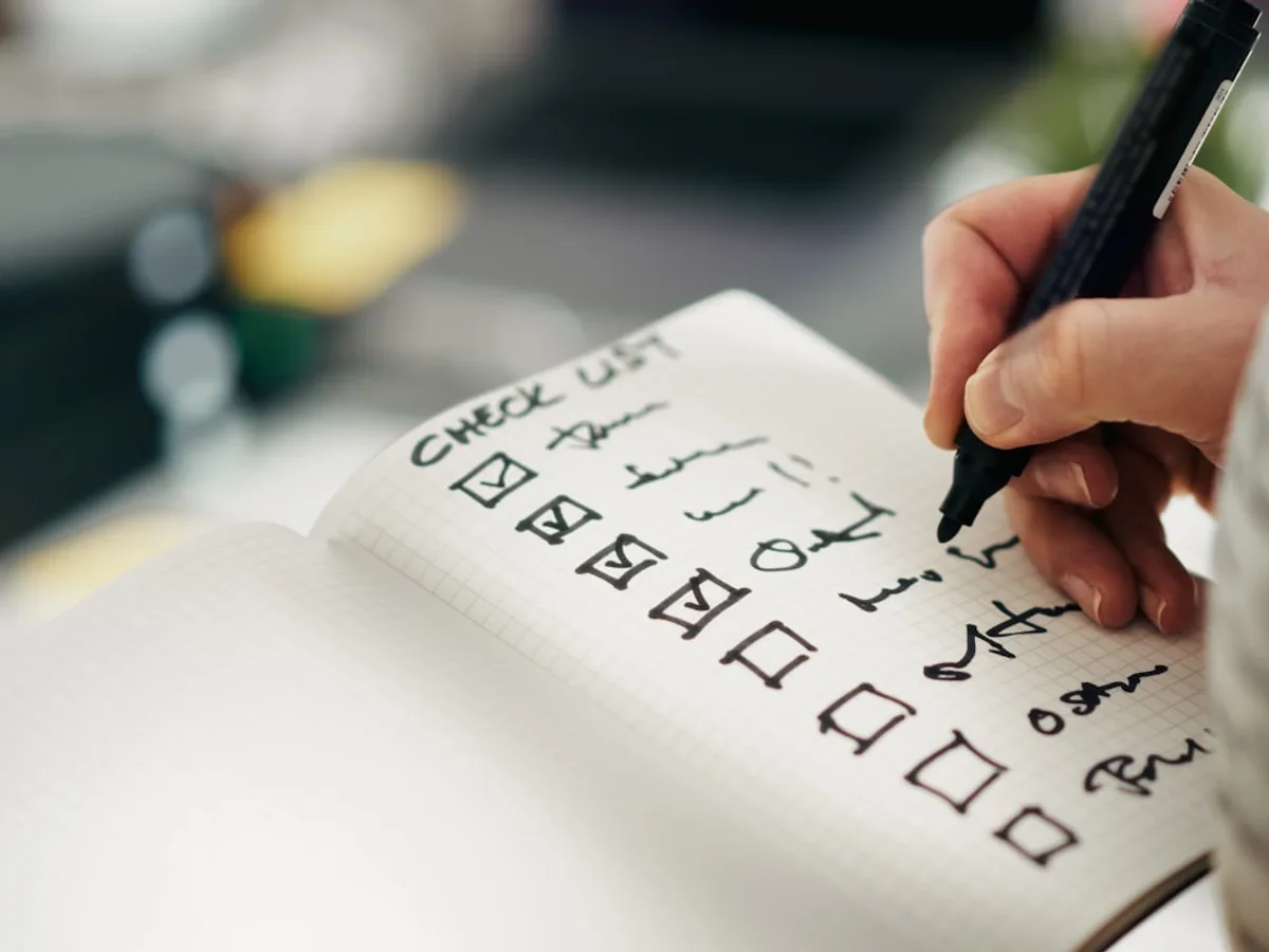 A hand marking checkboxes on a handwritten checklist in a notebook, representing GiveTurn's software quality assurance service
