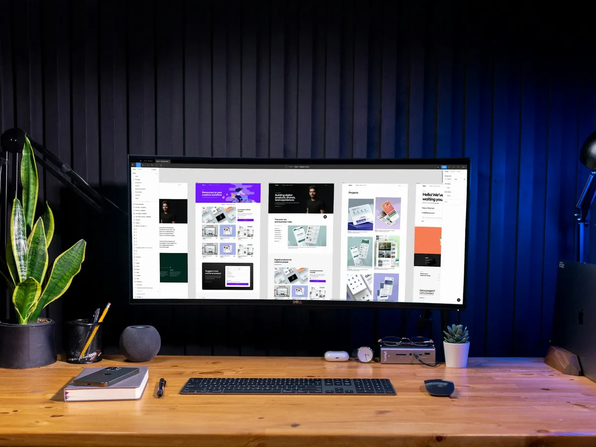 Widescreen monitor on a wooden desk displaying a colorful UI/UX design portfolio website, representing GiveTurn's UI/UX design service